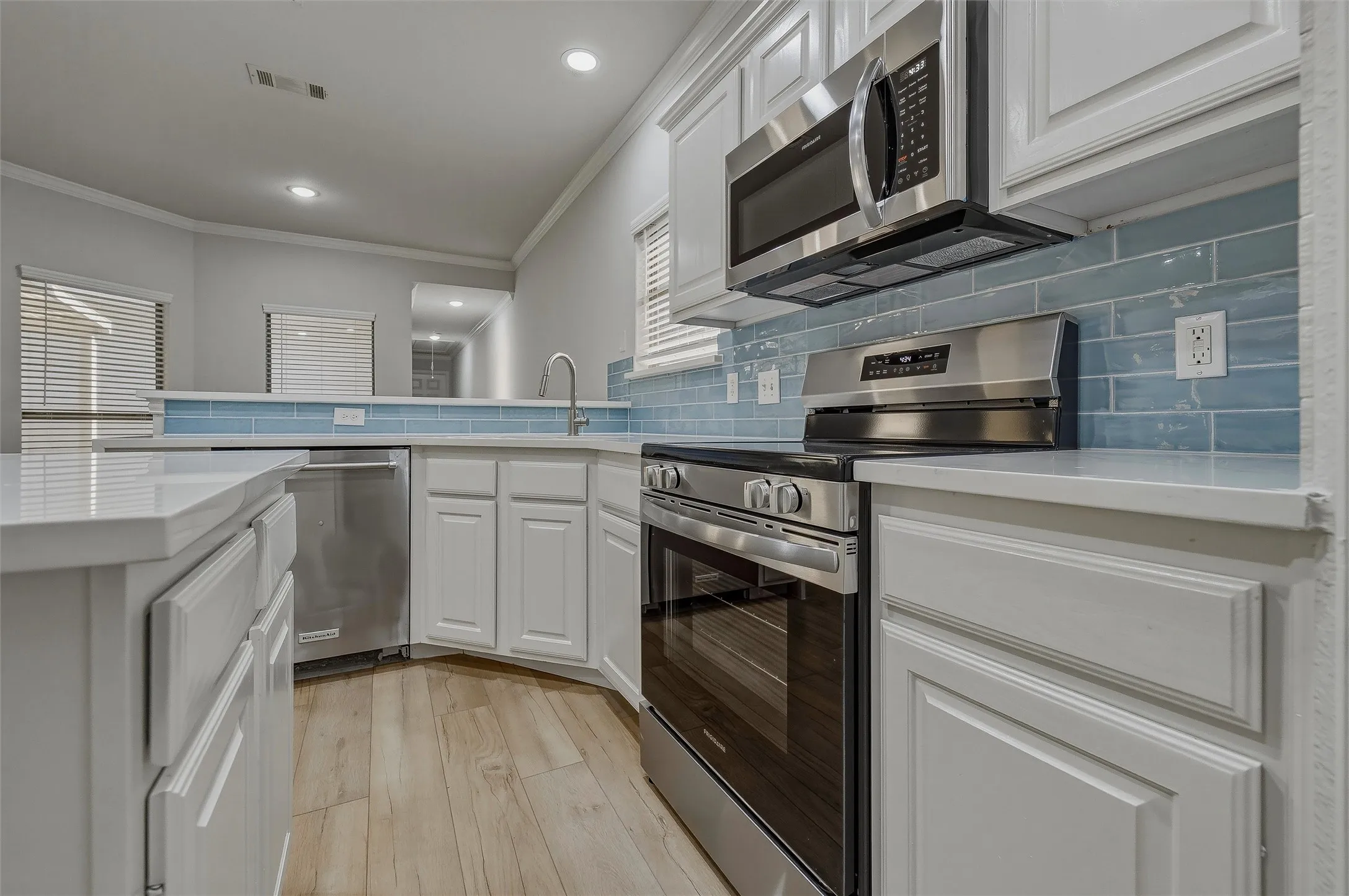 Kitchen featuring stainless steel appliances, light wood-finish flooring, white cabinetry, light blue subway tile backsplash, and recessed lighting