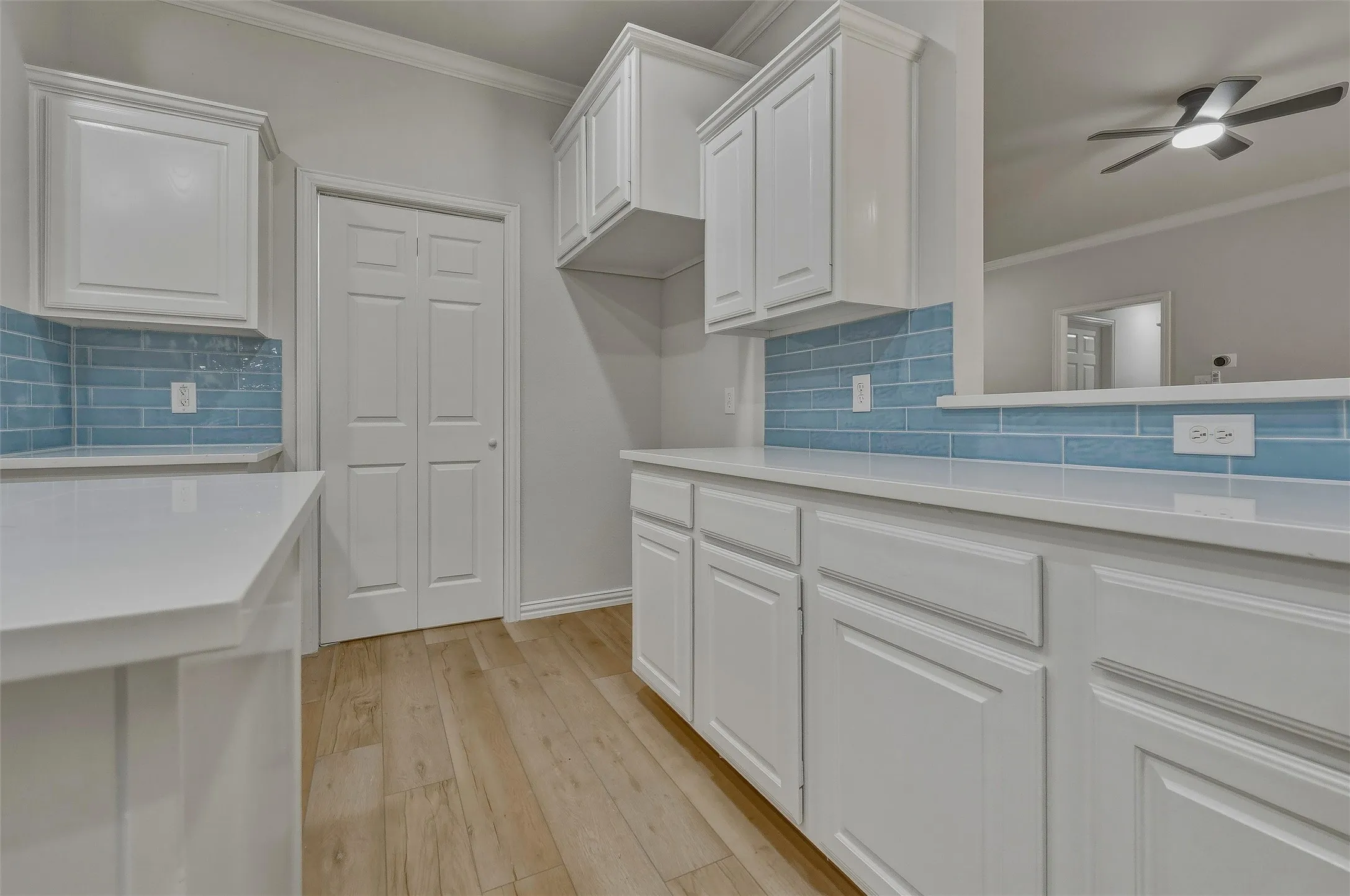 White cabinetry, light countertops, blue subway tile backsplash, wood-finish flooring, and a ceiling fan with integrated lighting