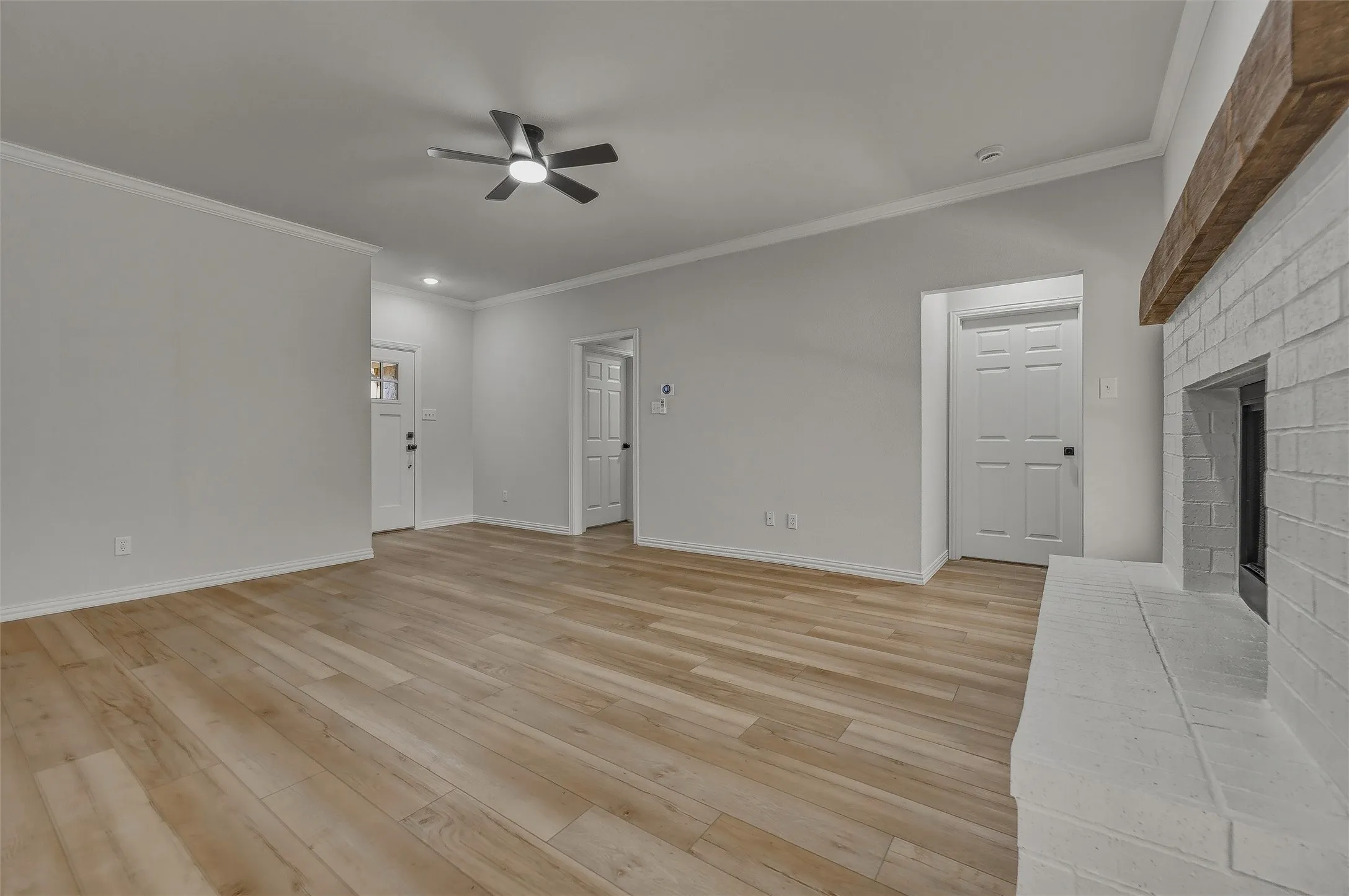 Wood-finish flooring, white brick fireplace with timber mantel, crown molding, and recessed lighting