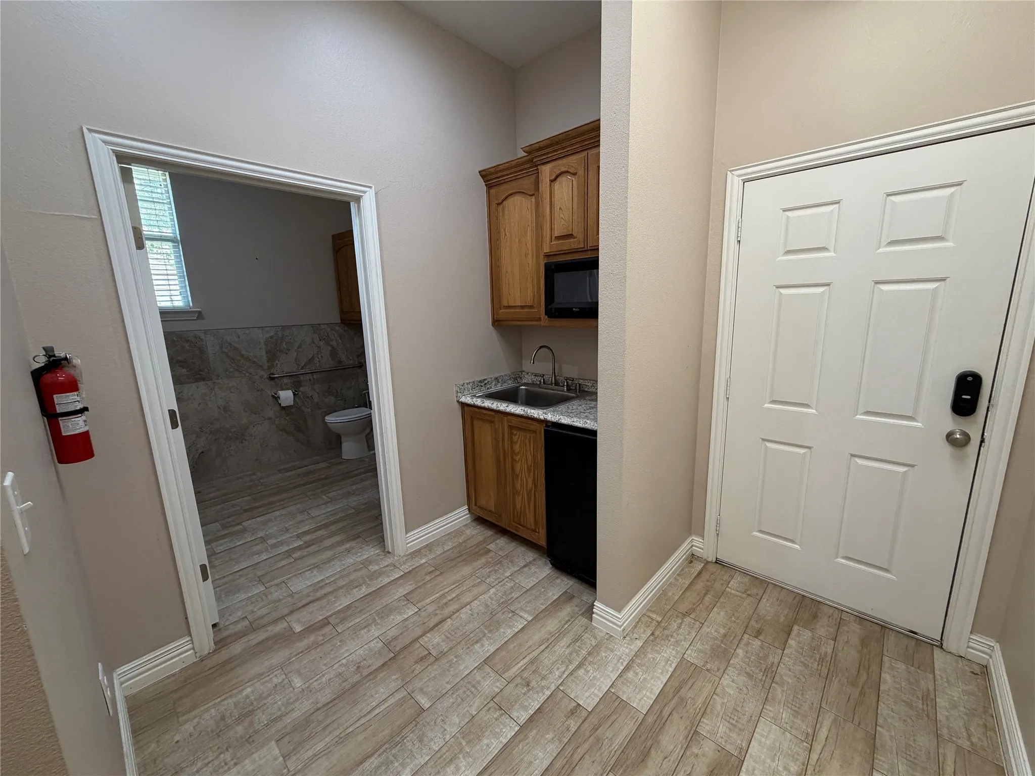 Wood-finish flooring, built-in kitchenette with wood cabinetry, integrated microwave, compact refrigerator, and granite-style countertop