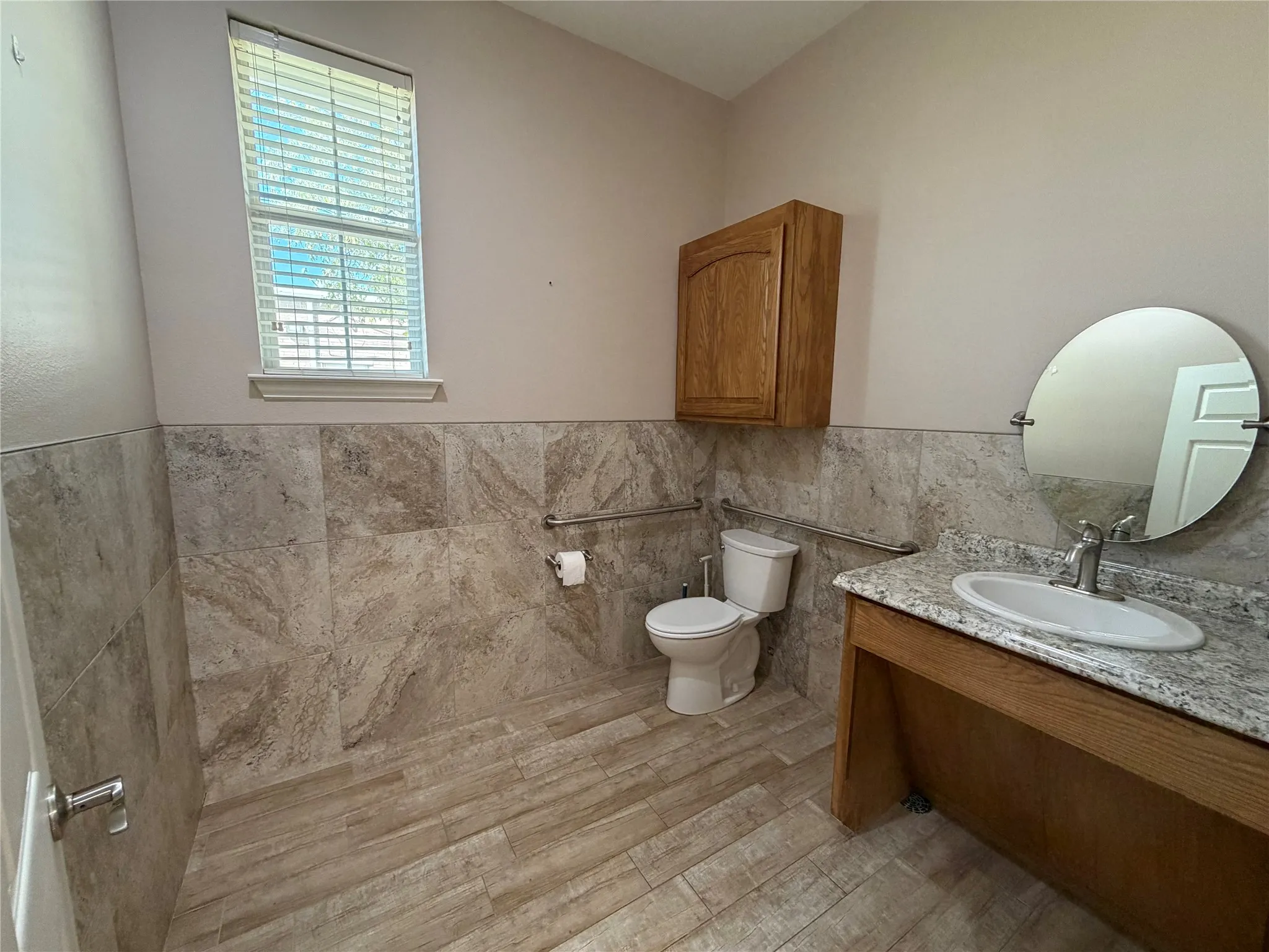 Tiled flooring and wainscoting, a single vanity with a granite-style countertop, and an oval mirror