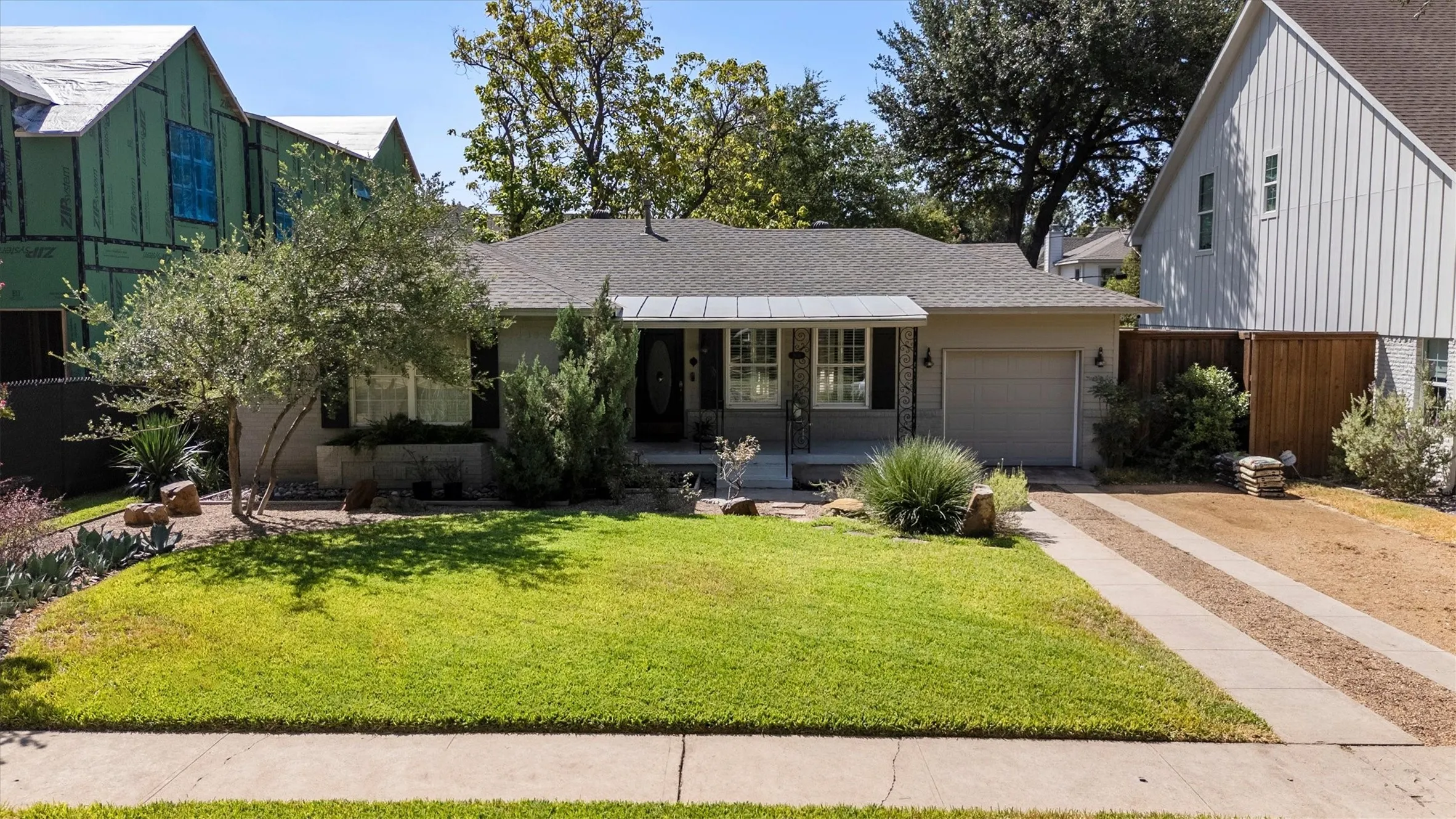 Single-story residence featuring a gray exterior, a two-car garage, a manicured front lawn, and established landscaping