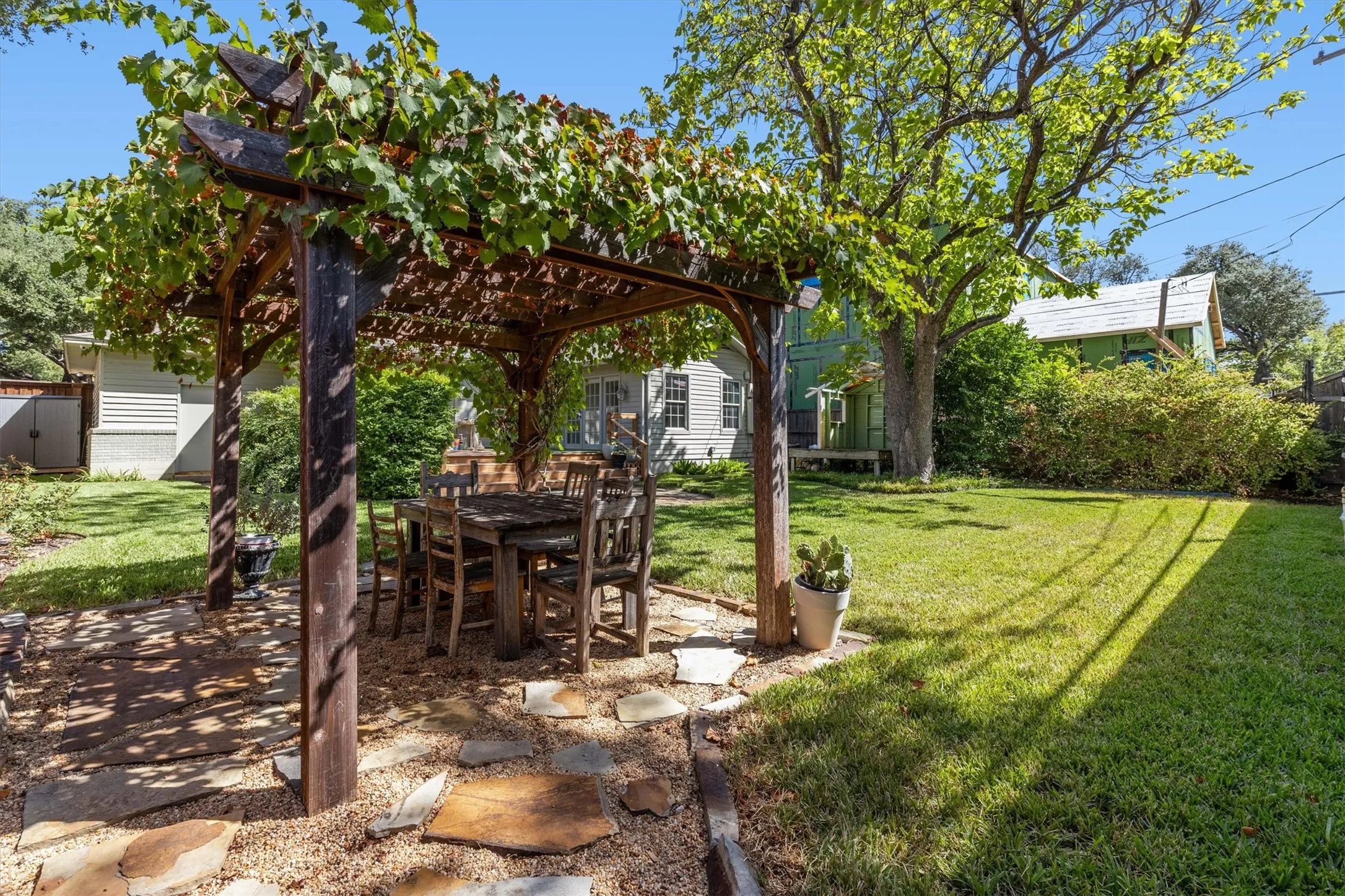 Wood pergola with overhead foliage, stone paver and gravel patio, and expansive lawn area