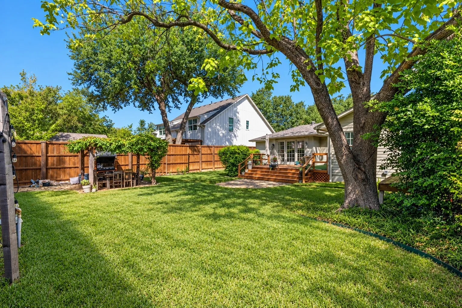 Expansive backyard featuring a manicured lawn, established shade trees, wood privacy fencing, and a multi-level wood deck