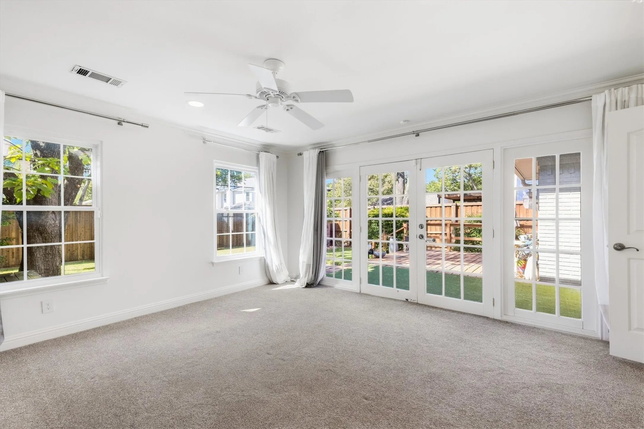 Plush carpeted flooring, white walls, two single-pane windows, and three French doors opening to an outdoor area