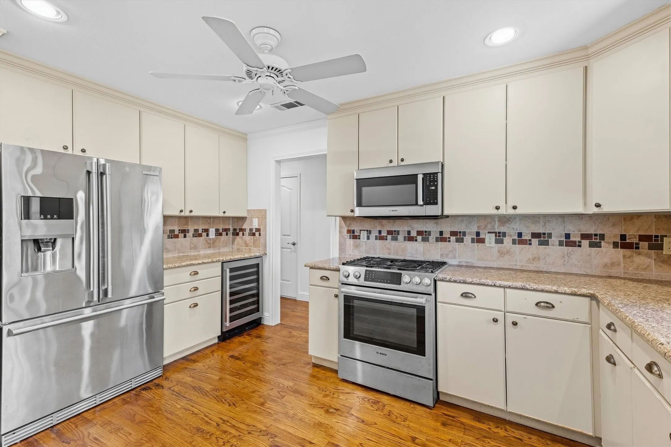 Stainless steel appliances, wood-finish flooring, white cabinetry, recessed lighting, and a ceiling fan