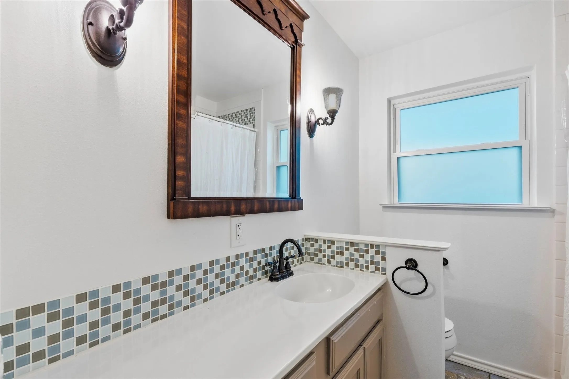Vanity with a single basin, a mosaic tile backsplash, and a framed mirror