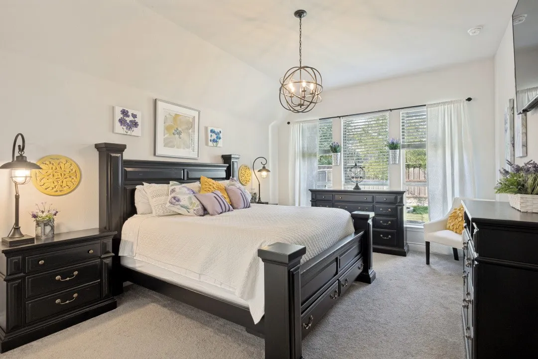 Vaulted ceiling with an orb chandelier, large window with blinds and curtains, and light gray carpet flooring