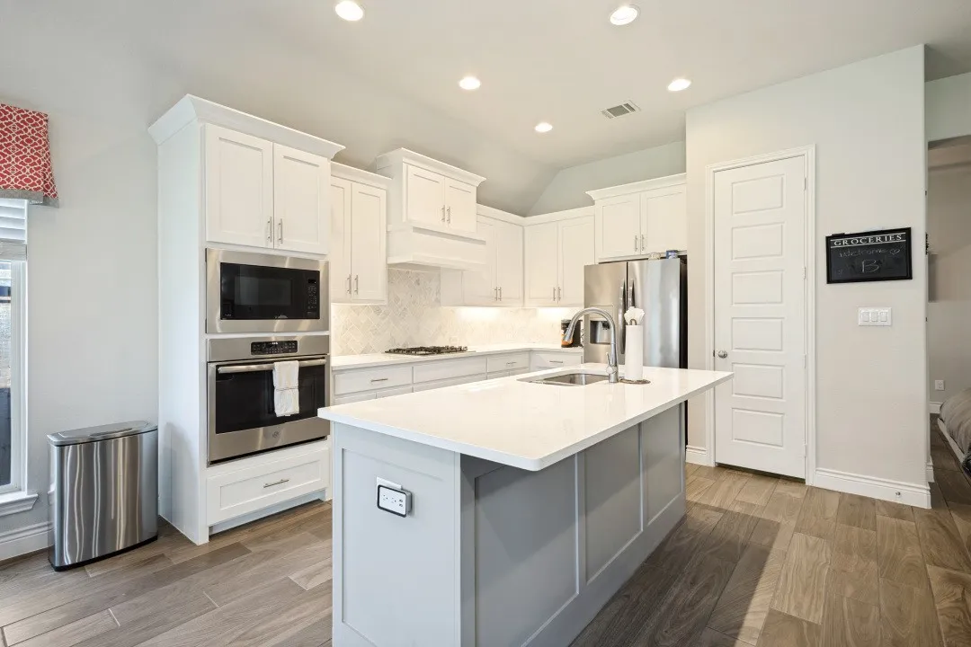 Kitchen featuring stainless steel appliances, white cabinetry, a center island with sink, light-colored countertops, and wood-finish flooring