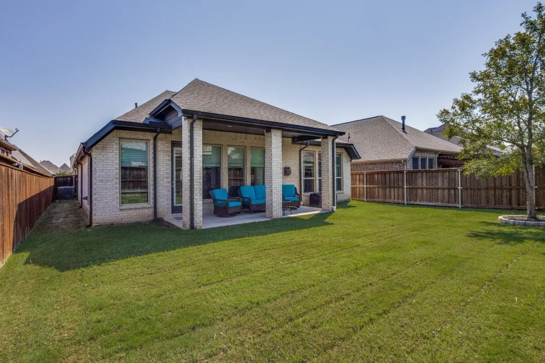 Expansive backyard featuring a manicured lawn, a covered patio, brick exterior, and a privacy fence