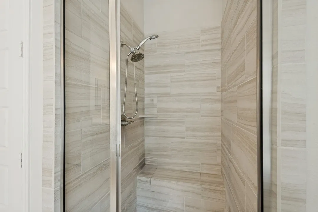 Glass-enclosed shower with a tiled bench seat, handheld shower fixture, and a built-in shower niche