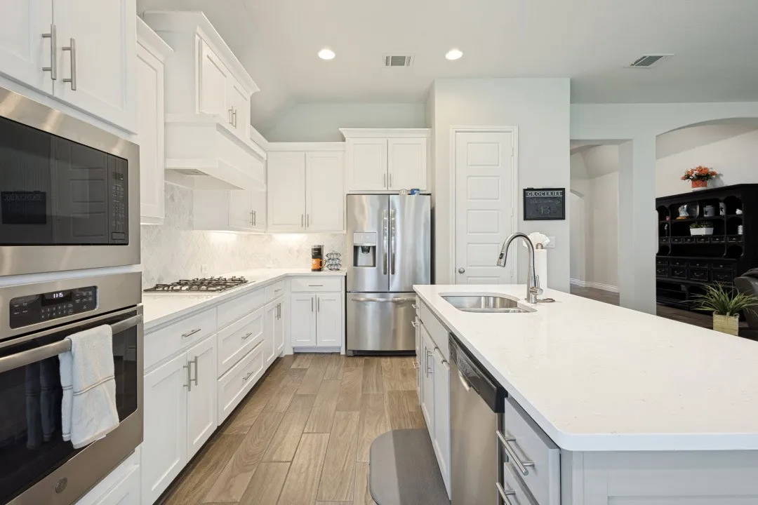 Stainless steel appliances, white cabinetry with crown molding, light-colored countertops, wood-finish flooring, and recessed lighting