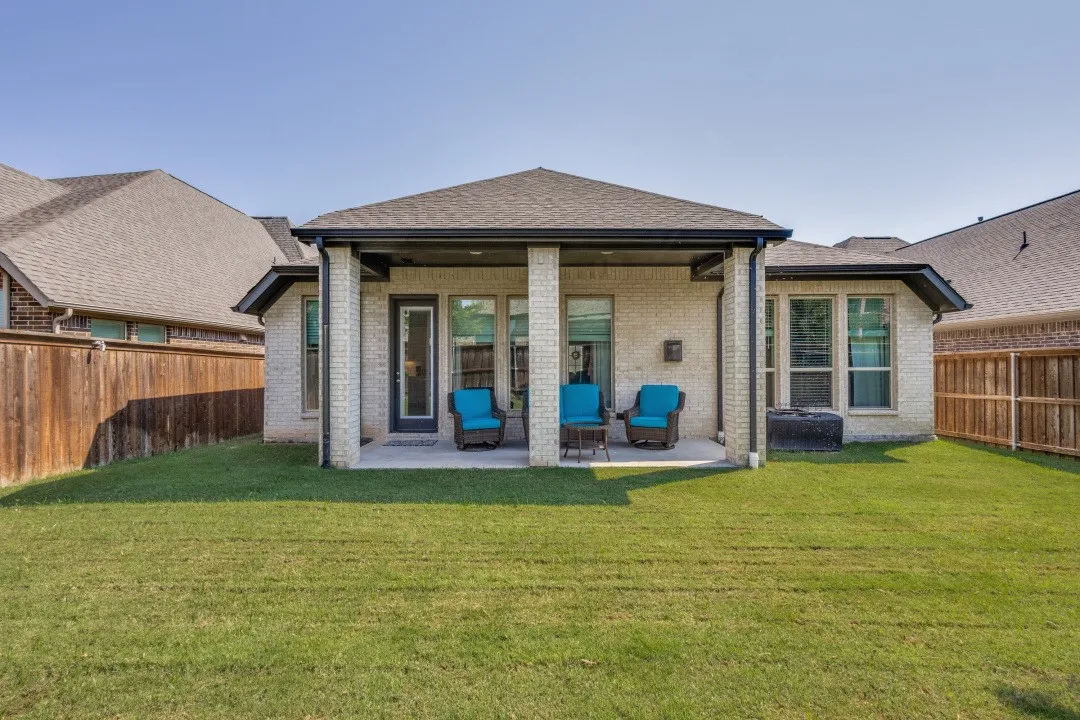 Expansive backyard with a covered patio, brick exterior, and a wood privacy fence