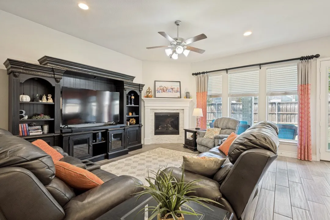 Wood-finish flooring, built-in entertainment center, recessed lighting, ceiling fan, and fireplace with mantle