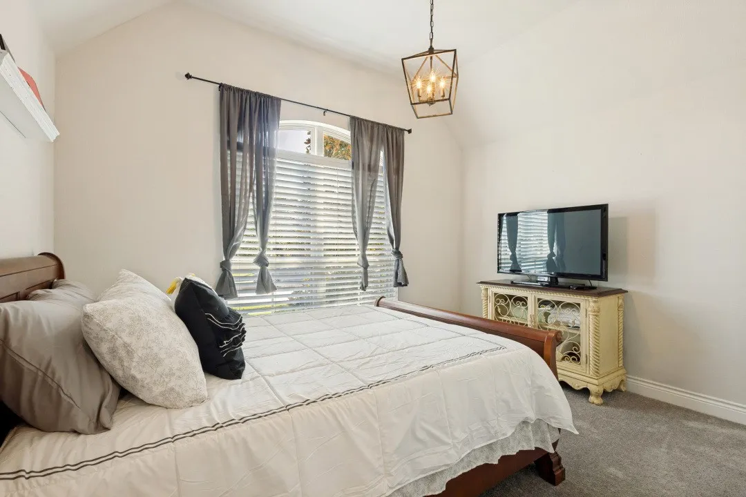 Vaulted ceiling with an industrial-style chandelier, arched window with horizontal blinds, and wall-to-wall carpeting