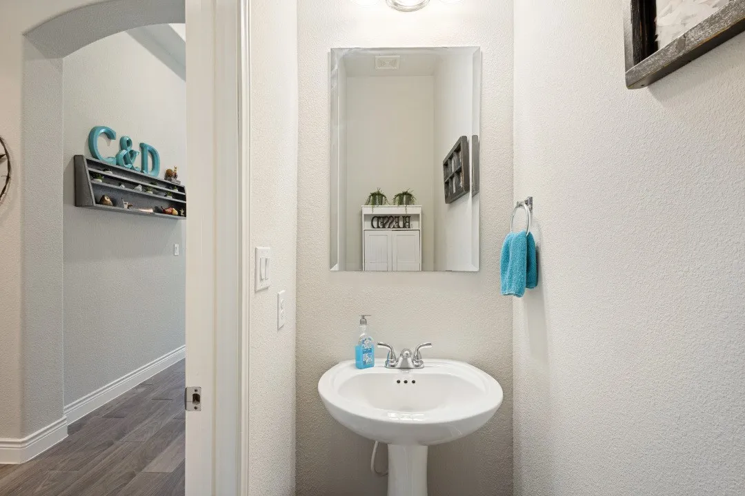 Pedestal sink with chrome faucet, rectangular wall mirror, and wall-mounted towel ring