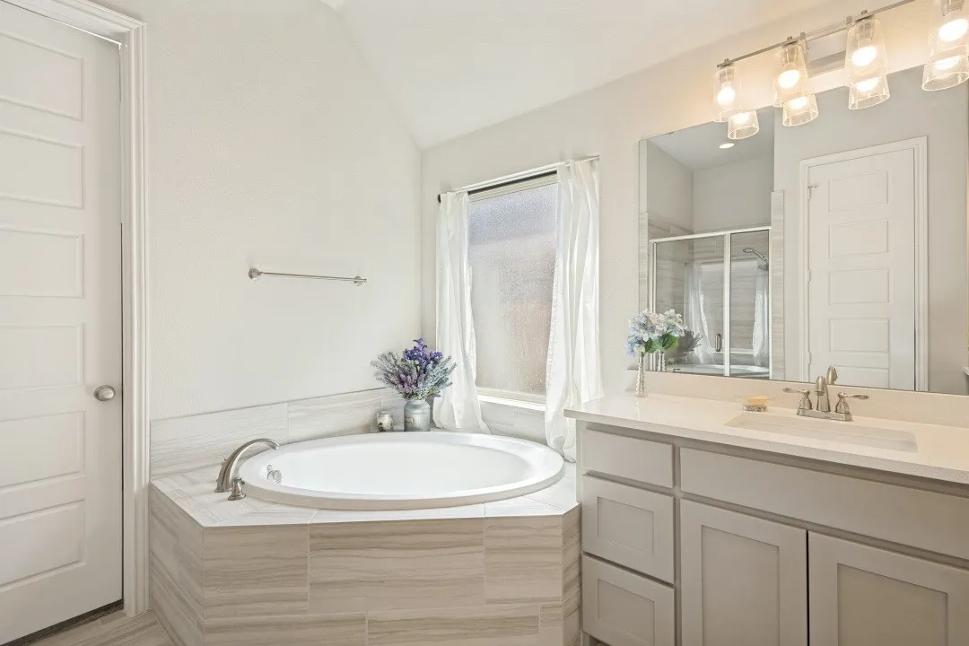 Built-in soaking tub with tile surround, double vanity with integrated sink, framed mirror, and a glass-enclosed shower