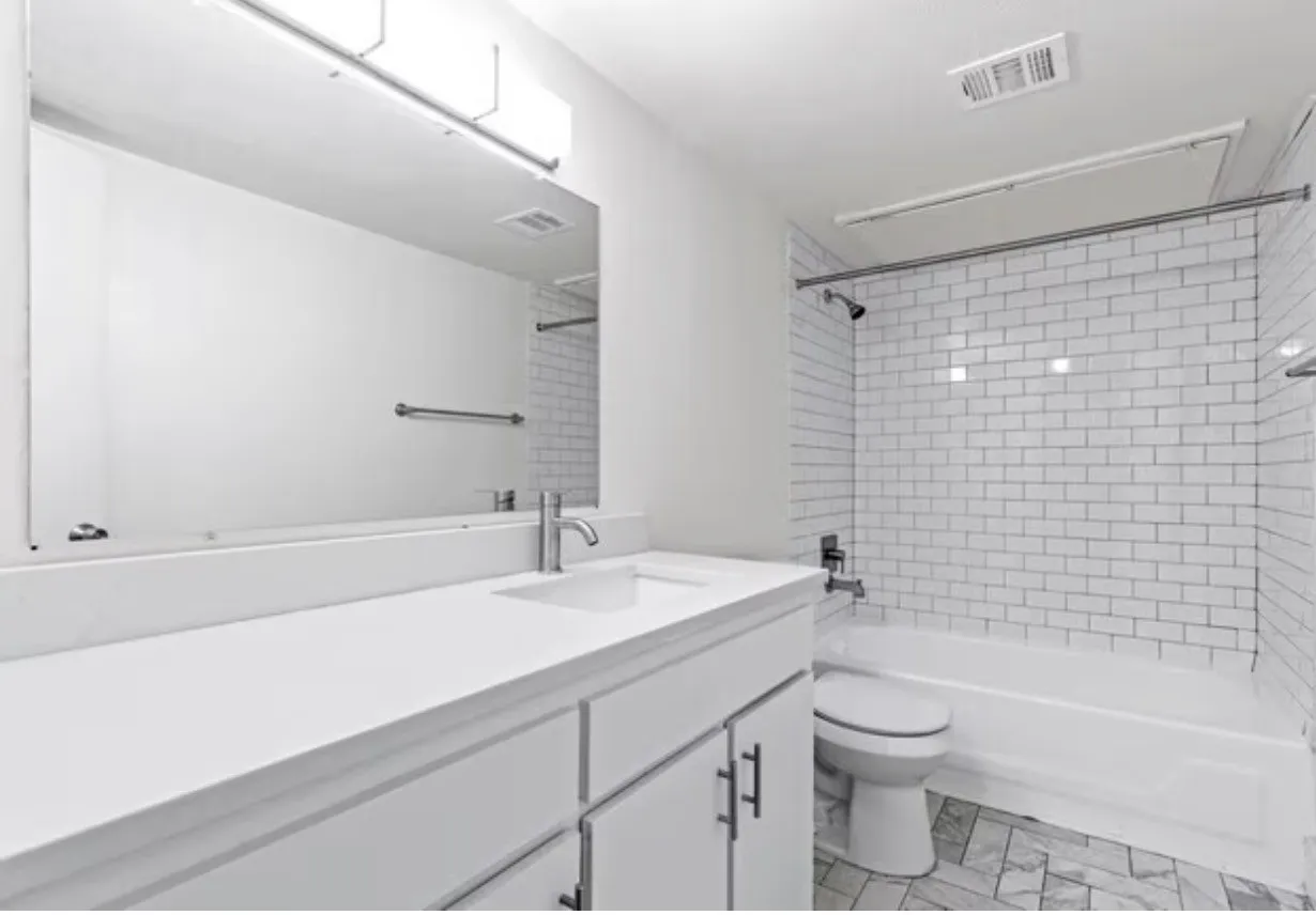 Bathroom featuring a single vanity with an integrated sink, white countertop, large mirror, subway tile shower surround, and patterned floor tile