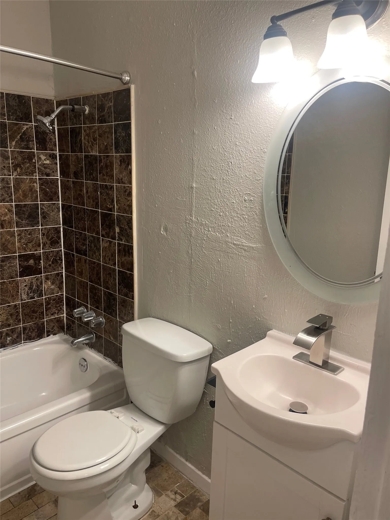 White bathtub with dark tile surround, white toilet, single vanity with integrated sink, and an overhead light fixture