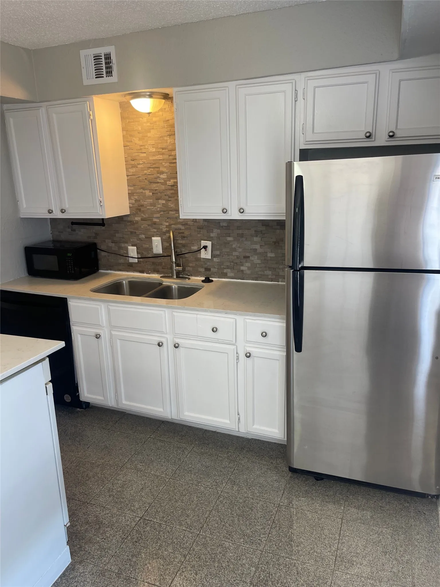White shaker-style cabinetry with circular hardware, stainless steel refrigerator, dual basin sink with a high-arch faucet, and a stone-finish tile backsplash