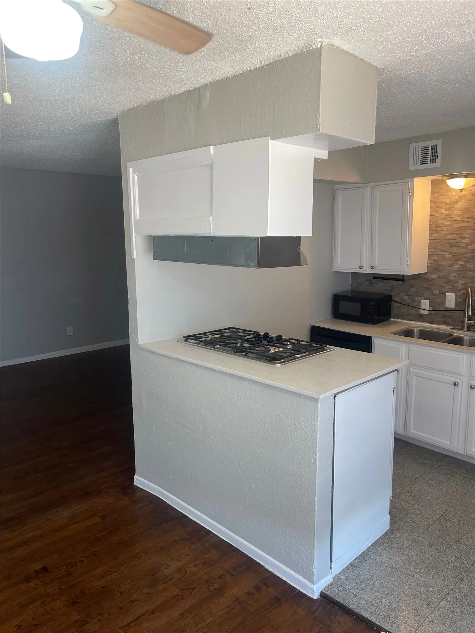 Kitchen featuring white cabinetry, light-toned countertops, a built-in cooktop, and a tile backsplash
