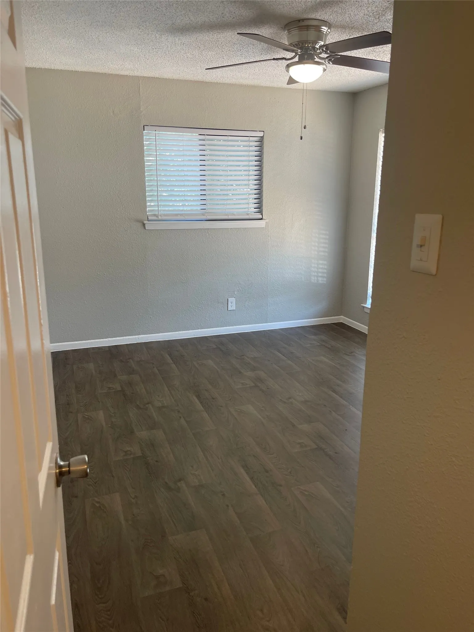 Wood-finish flooring, ceiling fan with integrated lighting, window with horizontal blinds, and neutral wall tones