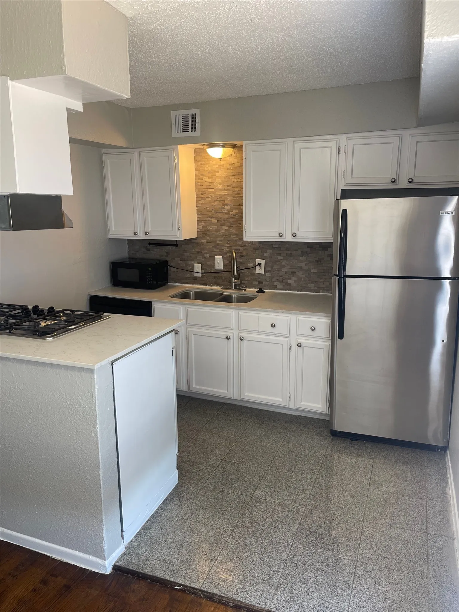 Kitchen featuring white cabinetry, a tile backsplash, stainless steel refrigerator, and a gas cooktop