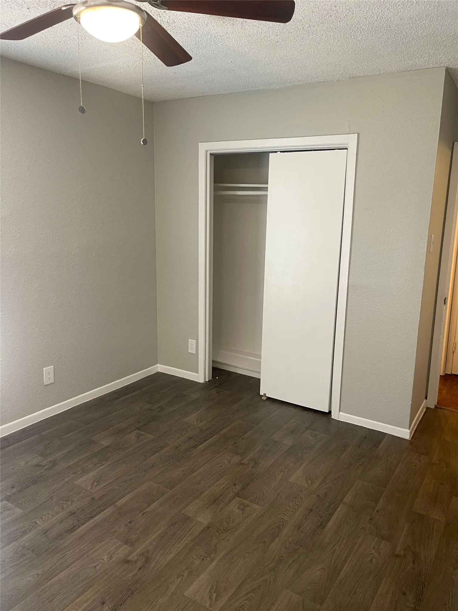 Wood-finish flooring, neutral wall tones, ceiling fan with integrated lighting, and a sliding closet door