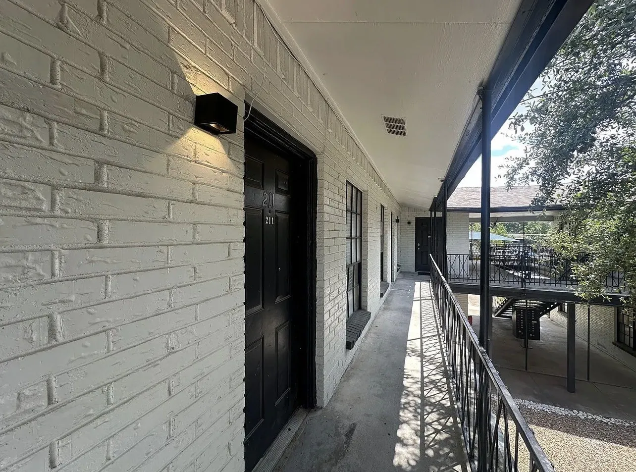 White painted brick exterior, black entry door, black exterior sconce, and black metal balcony railing