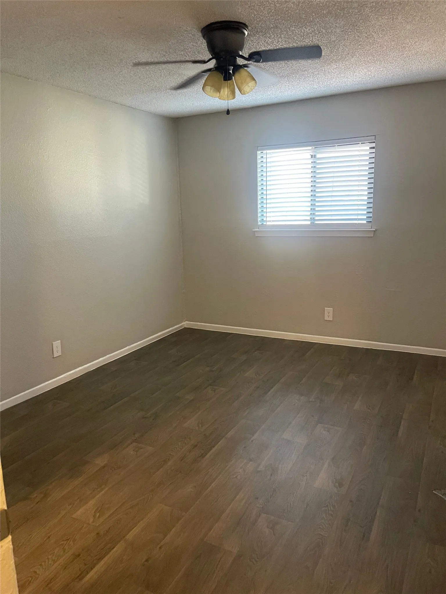 Wood-finish flooring, neutral wall tones, window with horizontal blinds, overhead ceiling fan with lighting, and white trim