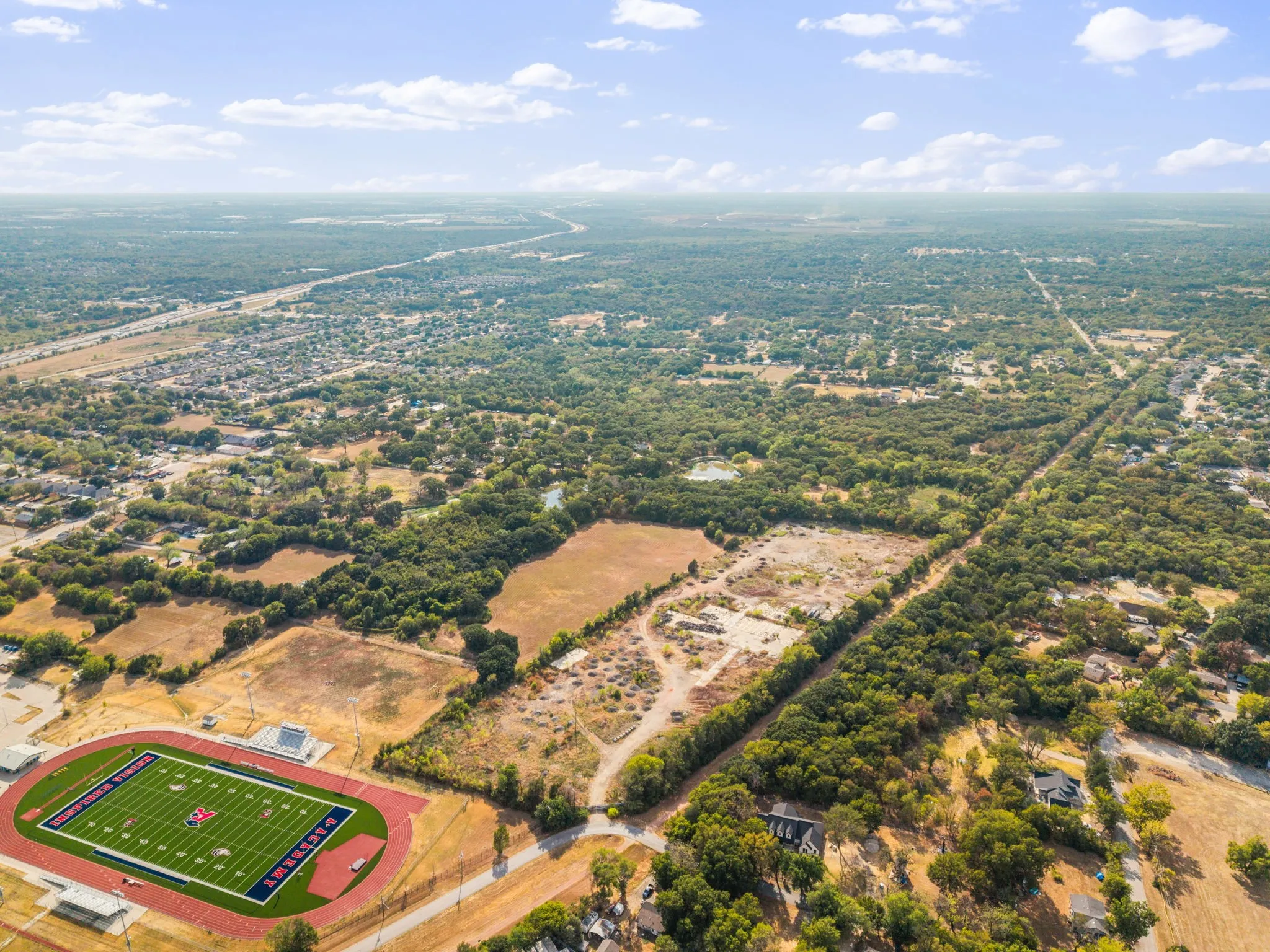 Expansive aerial perspective showcasing a football field with track, surrounding residential areas, and abundant mature trees