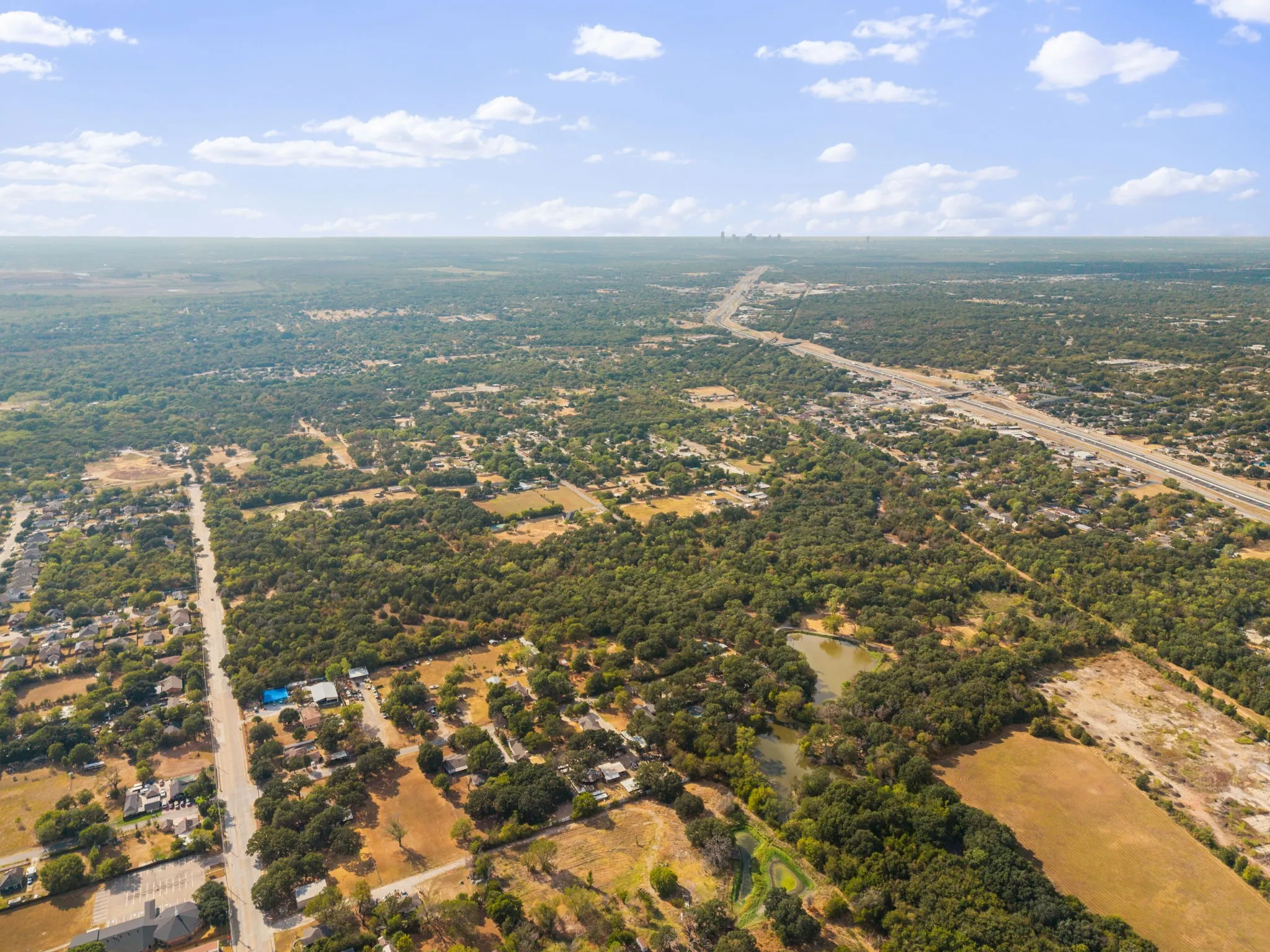 Expansive tree coverage, visible roadway infrastructure, and a natural pond feature