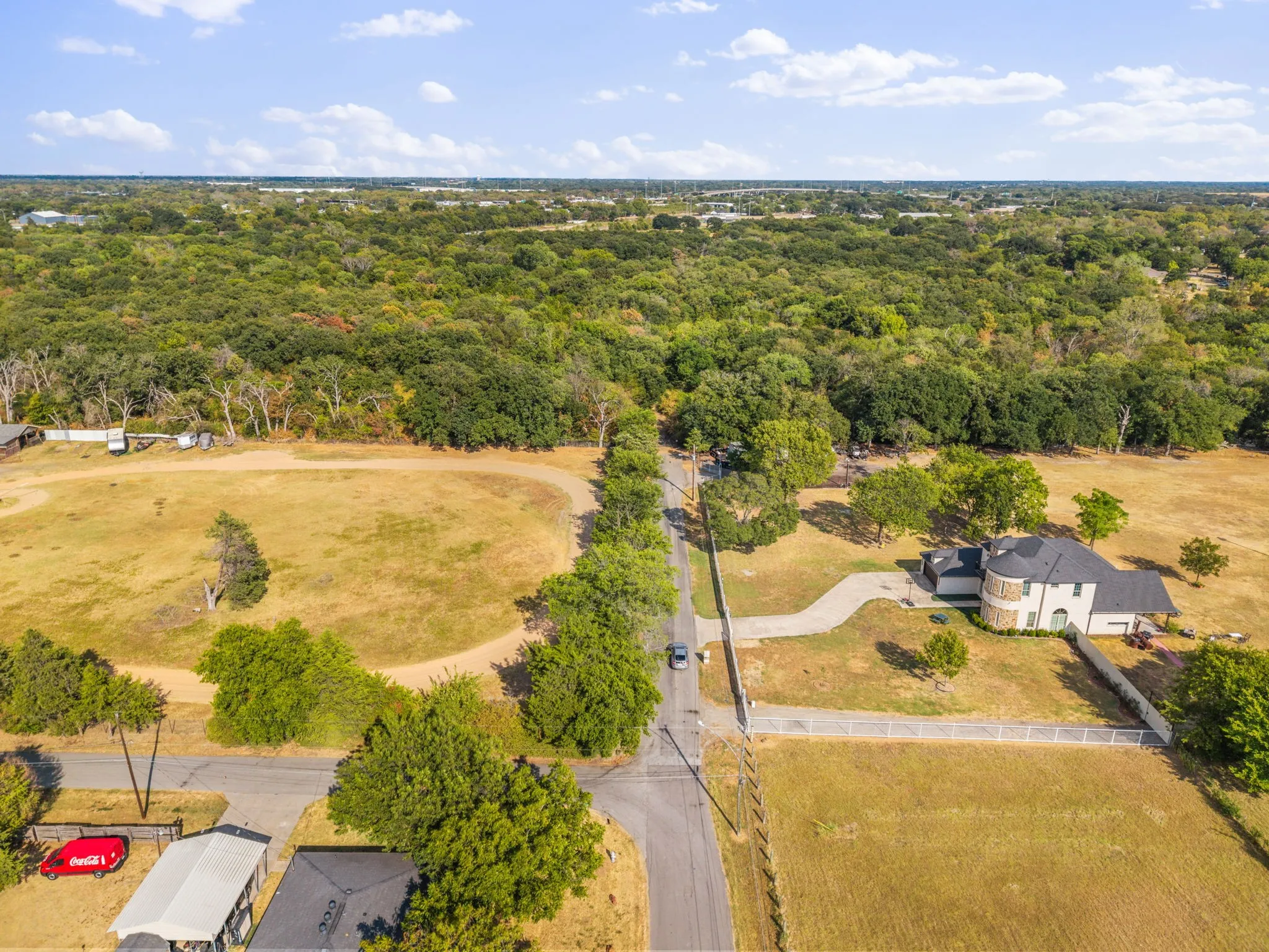 Expansive property featuring a large residence with a circular drive, surrounded by mature trees and open fields, bordered by a white fence
