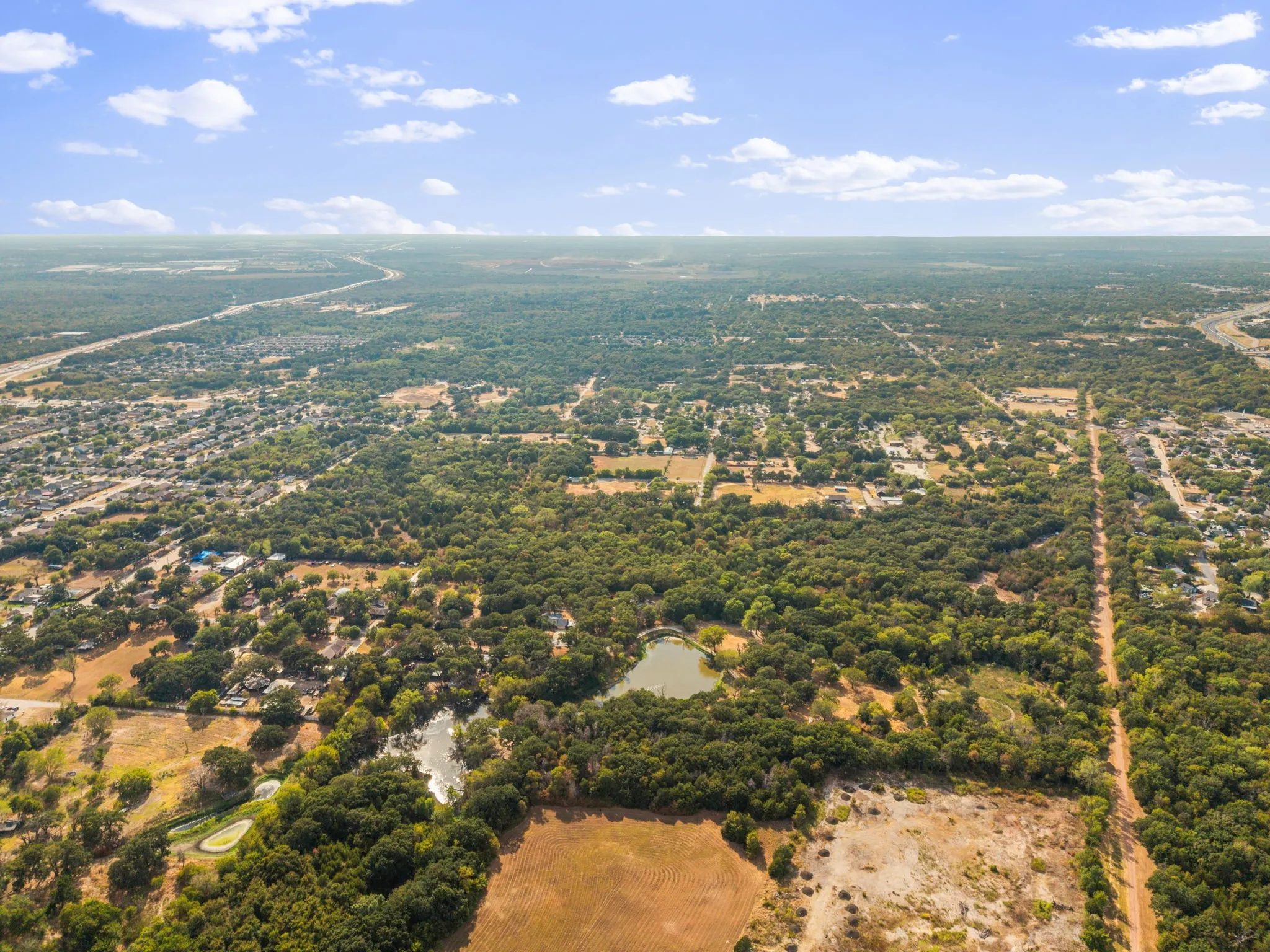 Expansive aerial landscape featuring a prominent pond, mature tree coverage, and surrounding residential areas