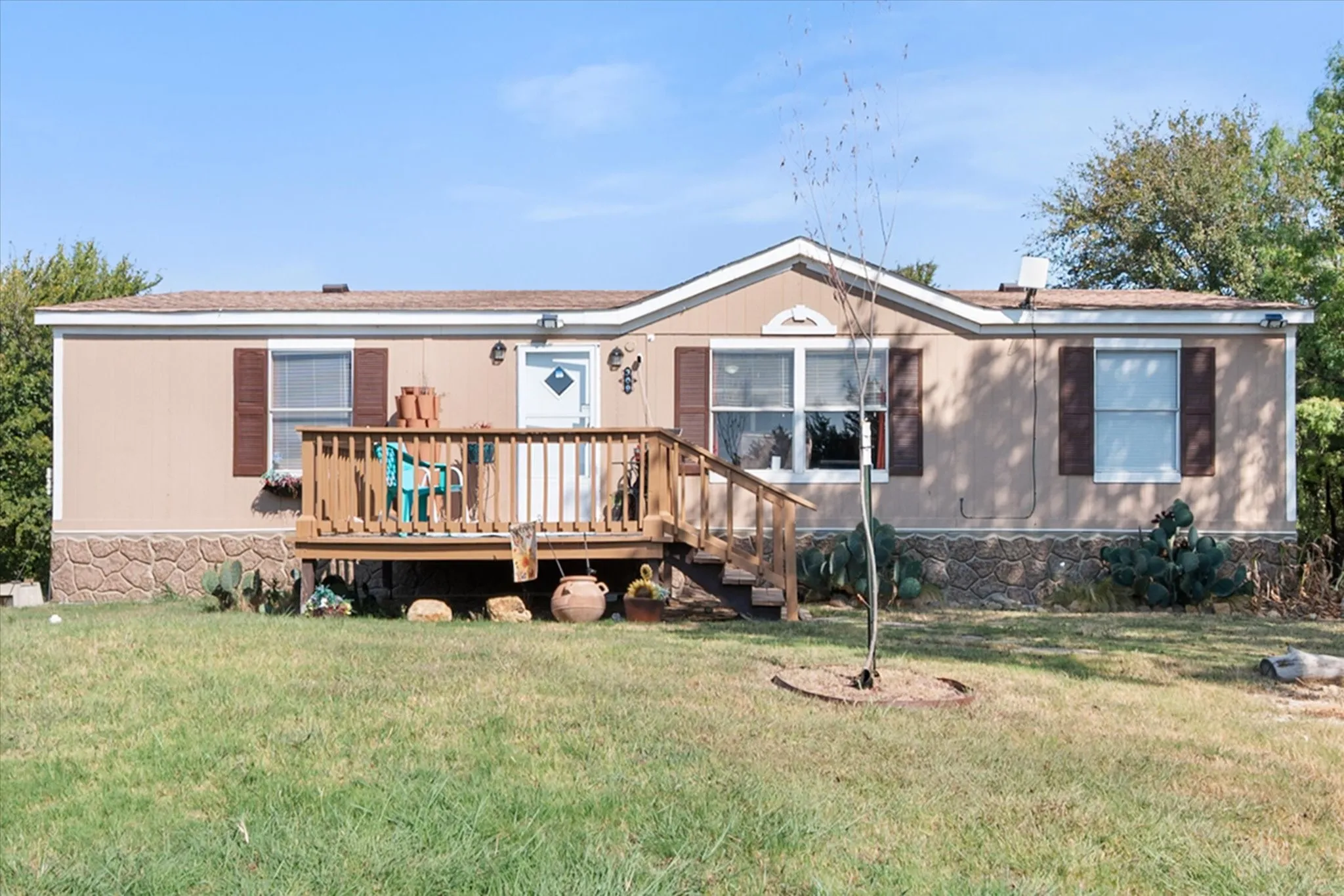 Front facade featuring a covered porch with wood railing, brown shutters, and stone-look foundation skirting