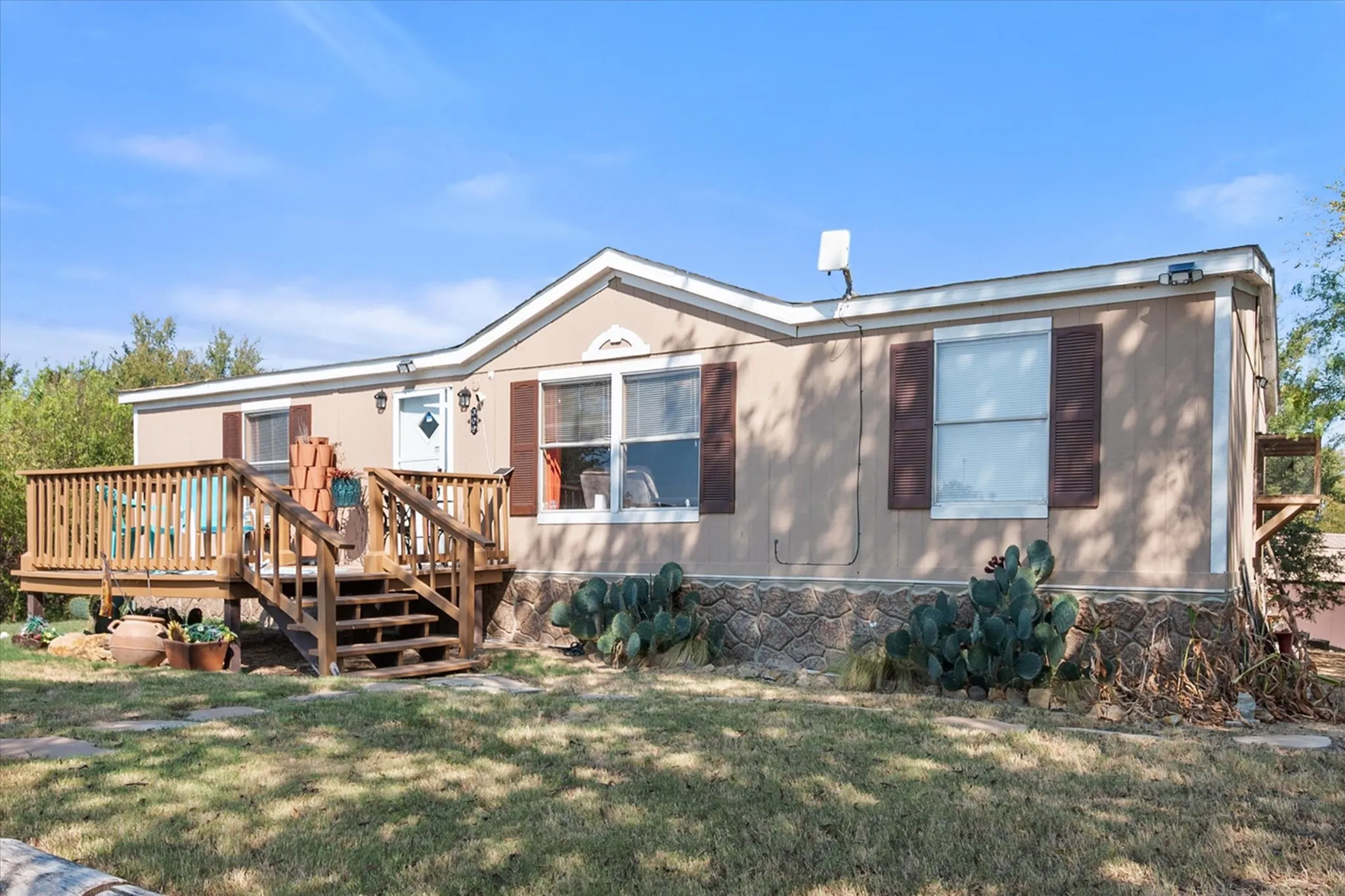 Exterior featuring a wood deck, stone-look foundation, and brown window shutters