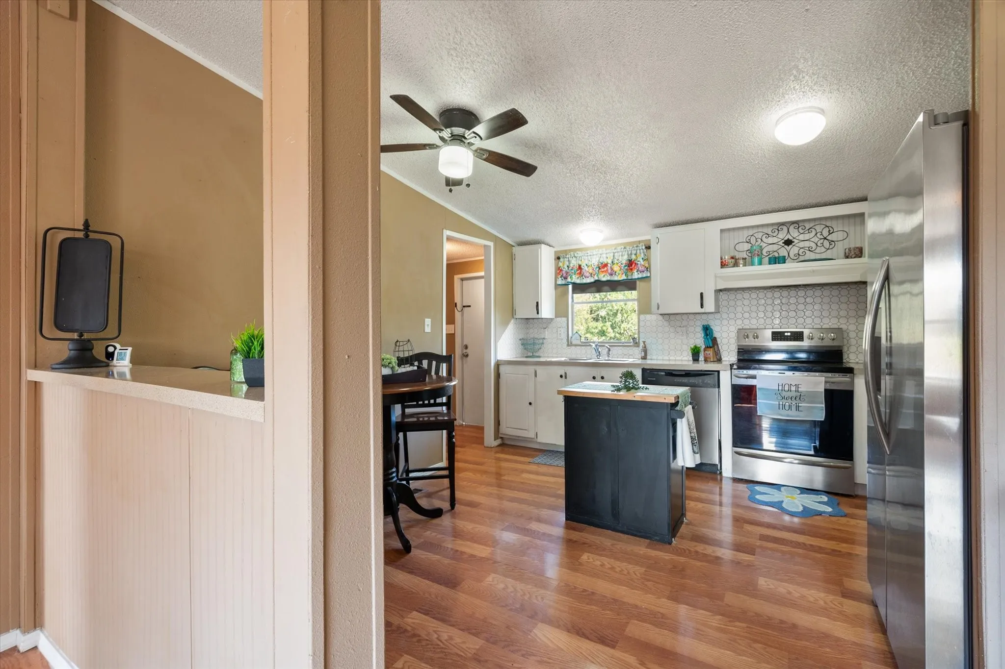 Wood-finish flooring, white cabinetry, stainless steel appliances, patterned tile backsplash, and a ceiling fan