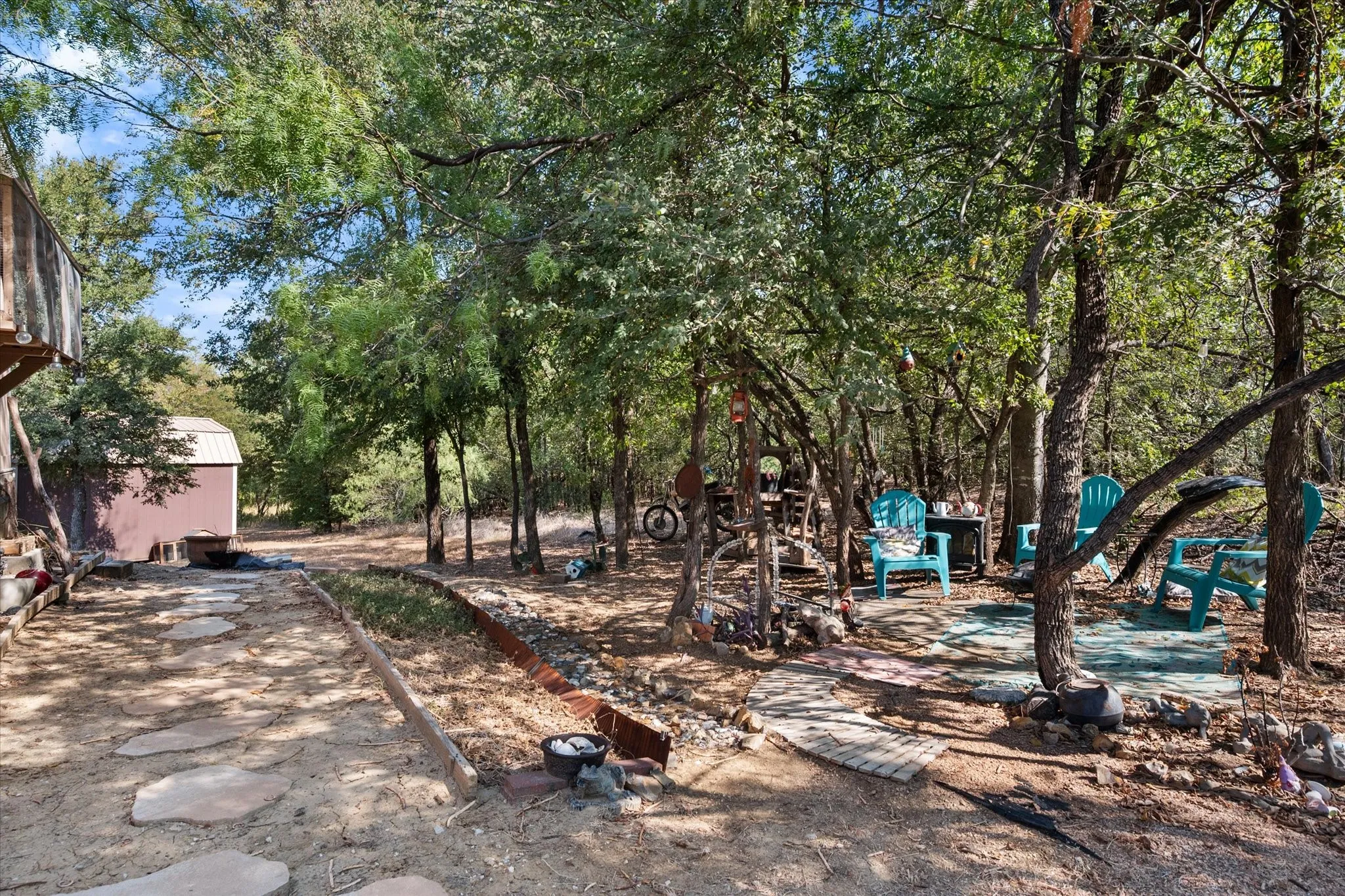Wooded lot featuring mature trees, a stepping stone walkway, and a storage shed