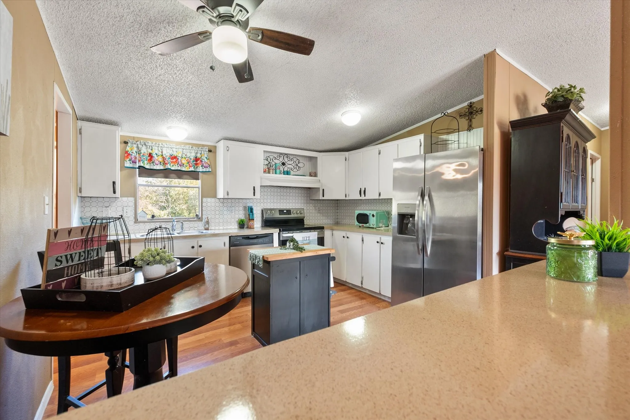 Kitchen featuring white cabinetry, stainless steel appliances, a center island, wood-finish flooring, and a ceiling fan