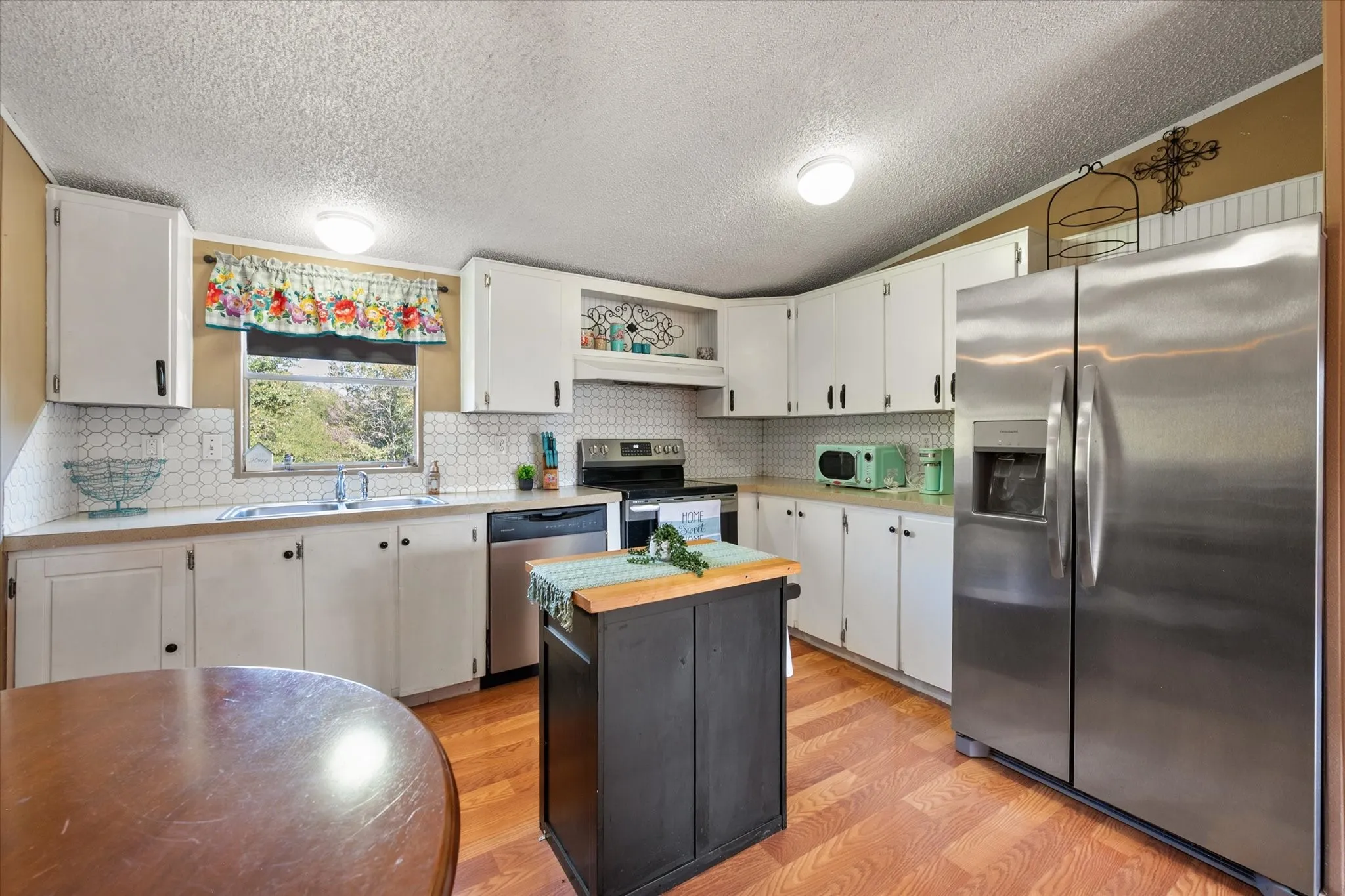 White cabinetry with dark hardware, stainless steel appliances, wood-finish flooring, white hexagonal tile backsplash, and a central island with a wood countertop