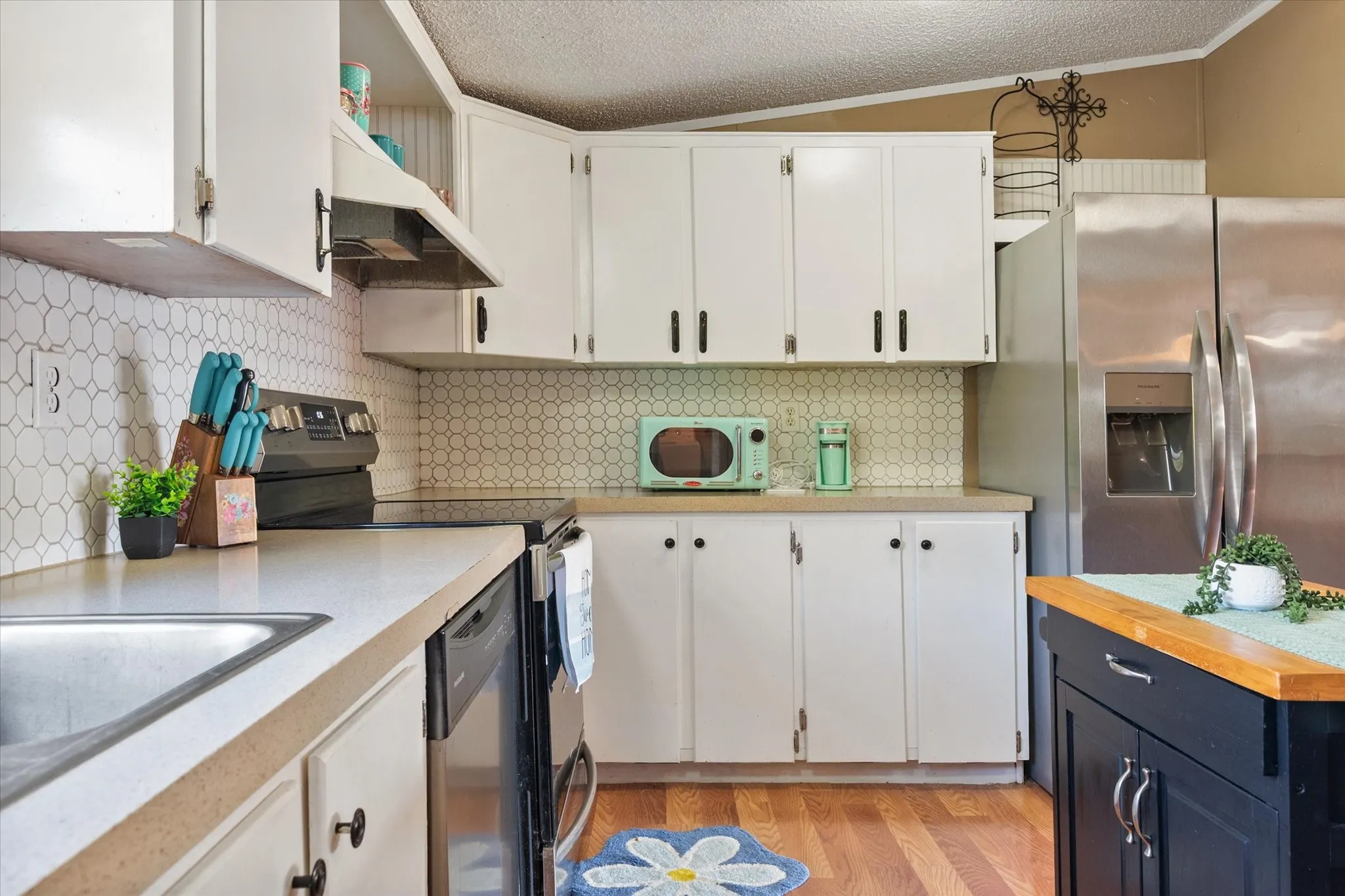 White cabinetry with dark hardware, full tile backsplash, stainless steel appliances, wood-finish flooring, and a kitchen island with a wood countertop