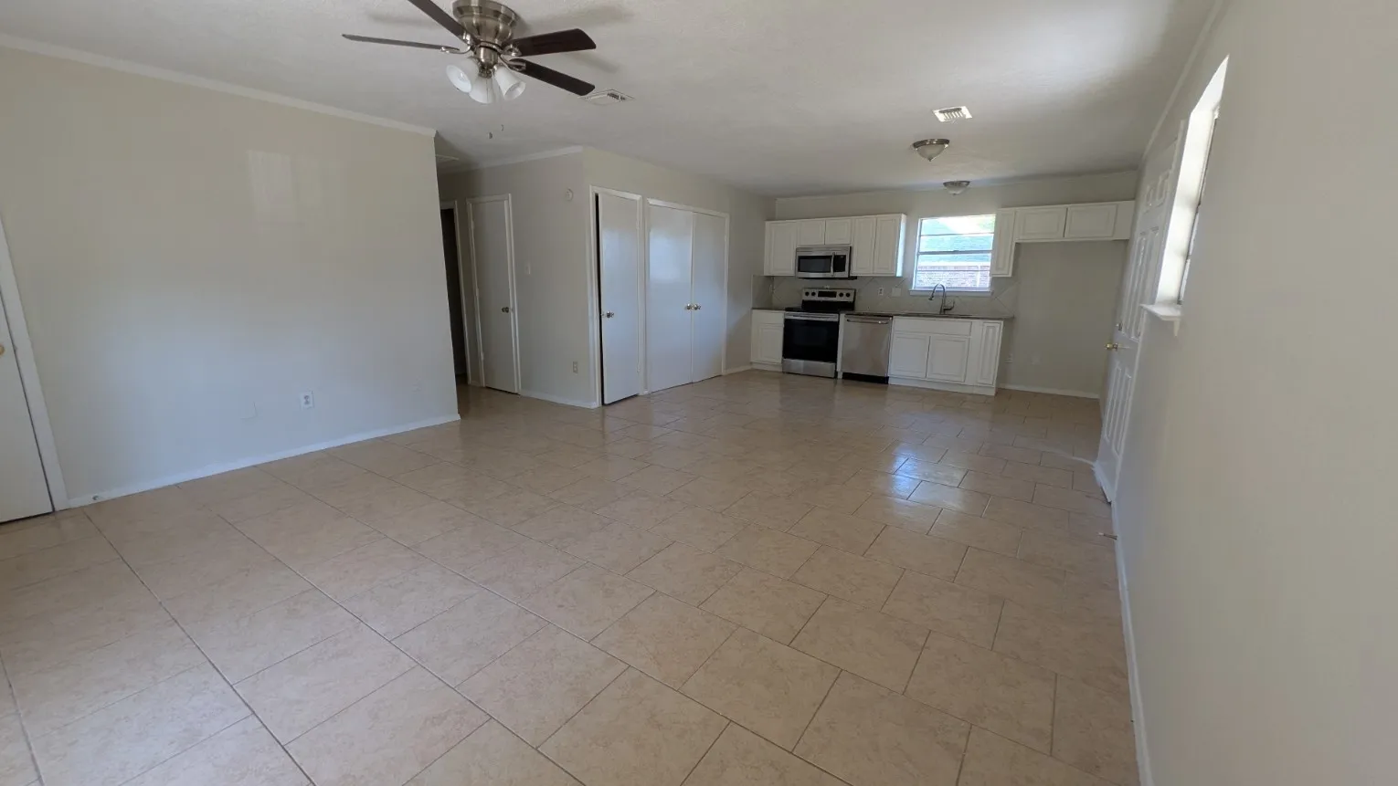 Open-concept living space featuring ceramic tile flooring, a ceiling fan, and white kitchen cabinetry with stainless steel appliances