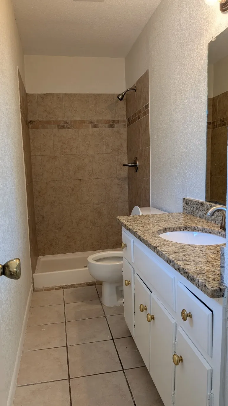 White vanity with brass hardware, granite-style countertop, and integrated sink
