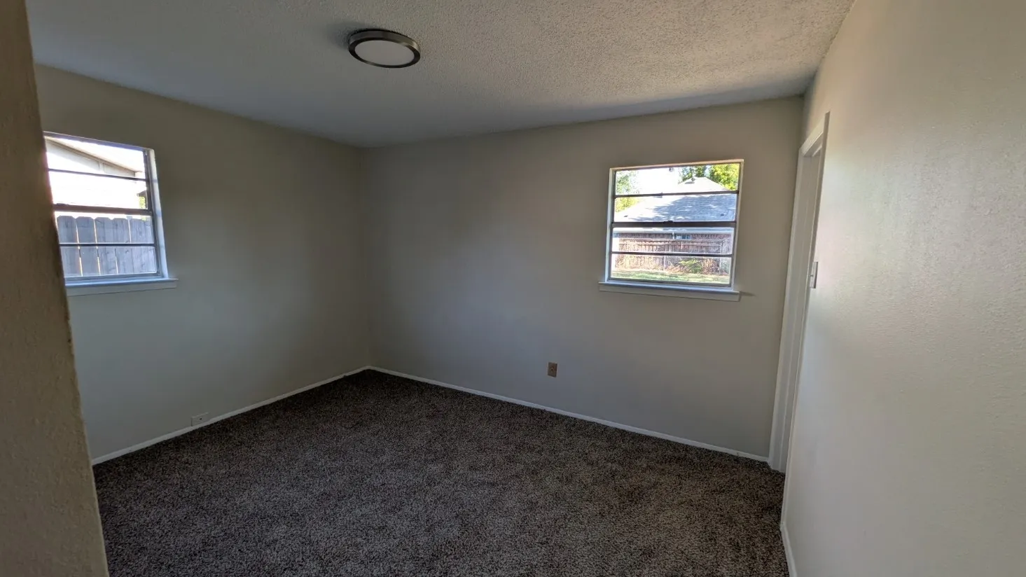 Carpeted flooring, neutral wall tones, two windows with blinds, and a flush-mount ceiling light fixture