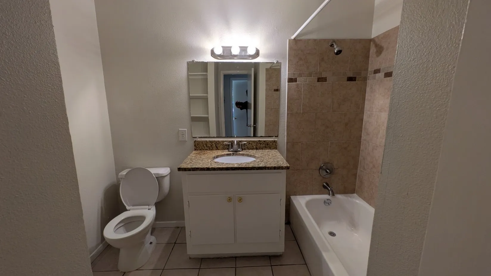 Bathroom with a combination shower and tub, tile surround, vanity with a built-in sink, and a granite-patterned countertop