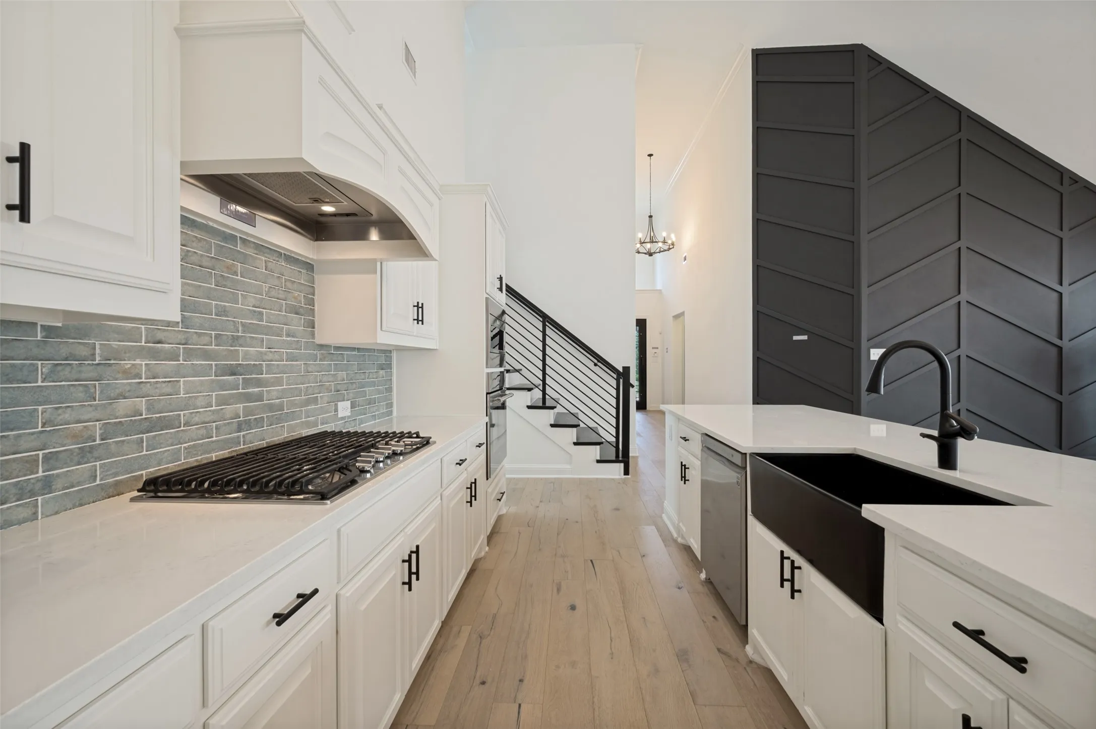 Kitchen featuring a gas range, light-toned brick-patterned backsplash, white cabinetry, integrated dishwasher, and a black farmhouse sink