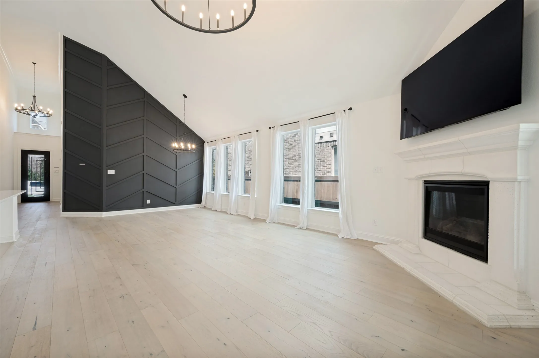 Vaulted ceilings with contemporary chandeliers, wood-finish flooring, a decorative accent wall, a fireplace with a mantel, and multiple windows