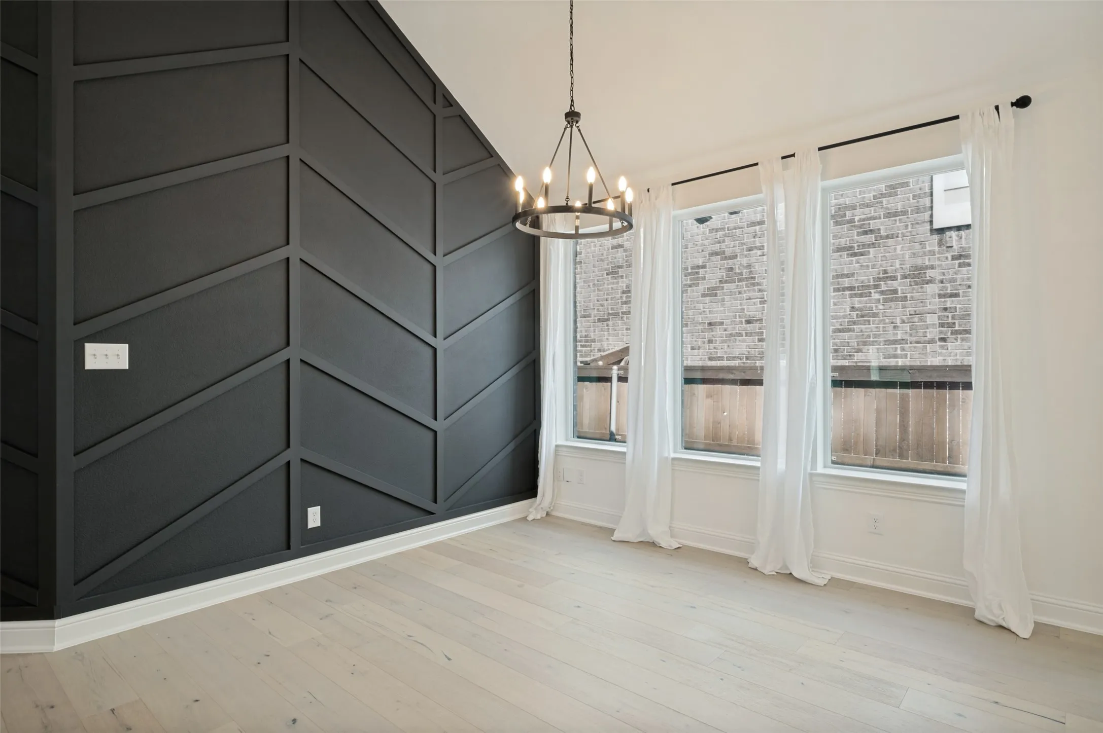 Accent wall featuring a chevron pattern, light wood-finish flooring, and a multi-bulb chandelier