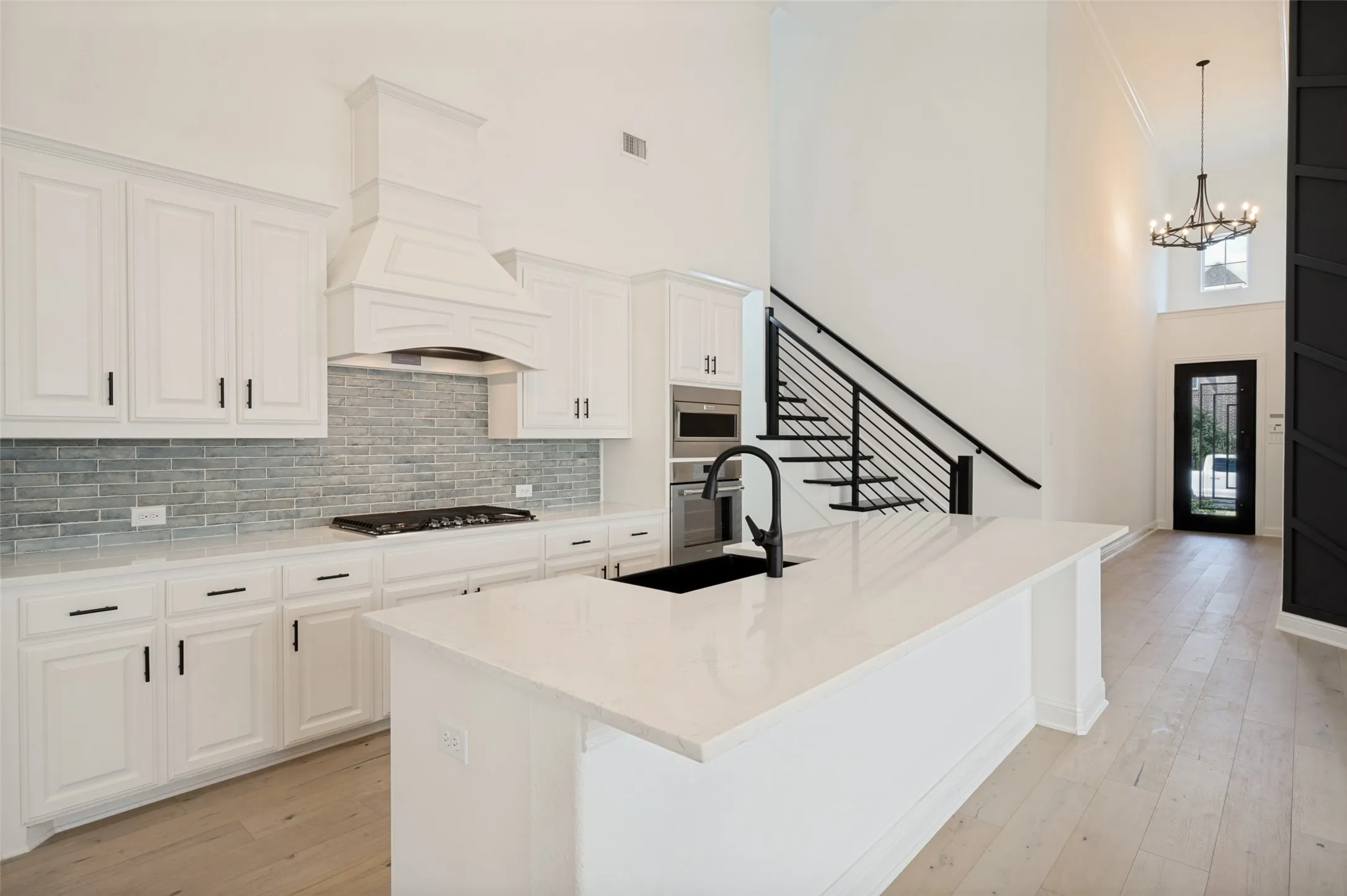 Kitchen with white cabinetry, quartz countertops, tile backsplash, and a large central island with sink