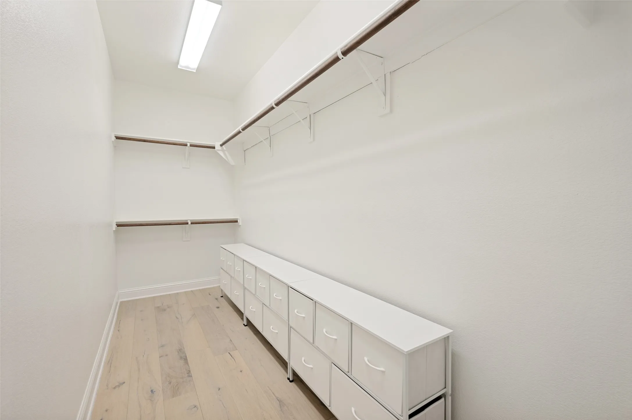 Walk-in closet with multiple hanging rods, overhead shelving, and wood-finish flooring